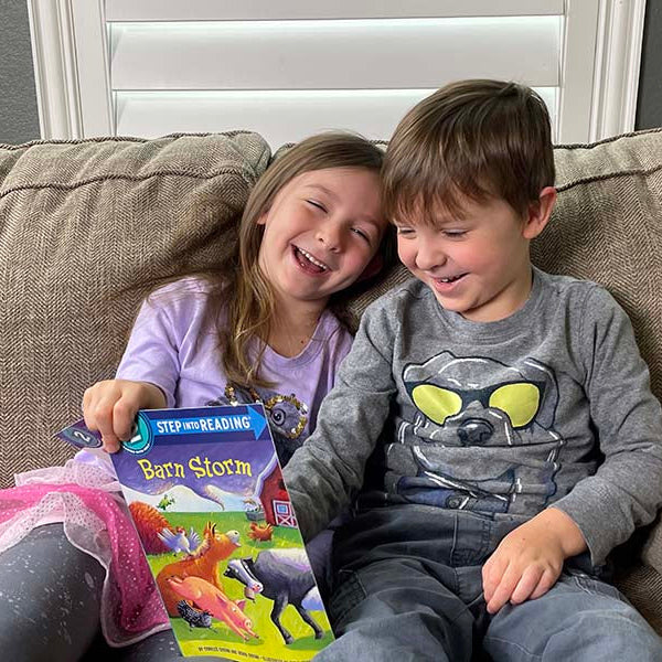 two laughing kids sharing a Barn Storm book together on a couch